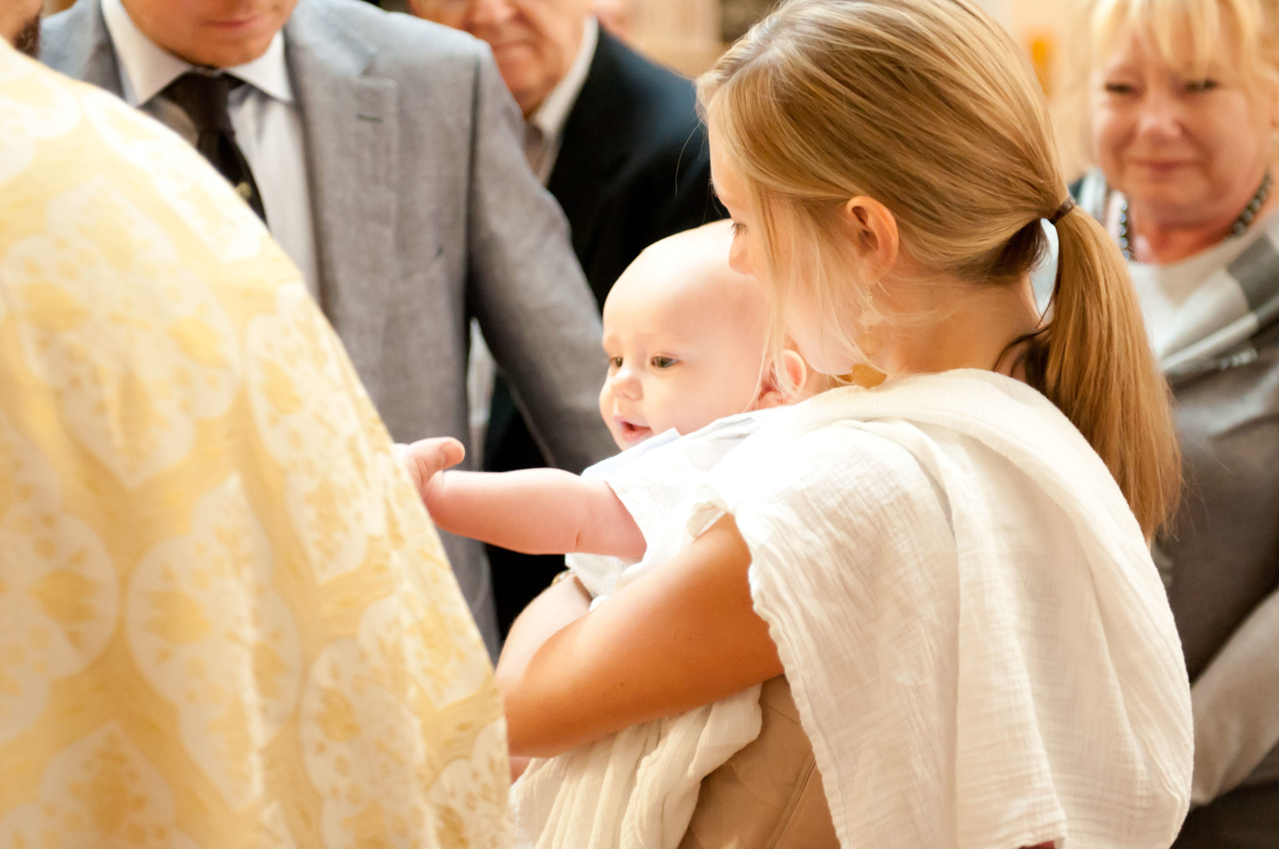 Baby reaching for priest at baptism in MPLS