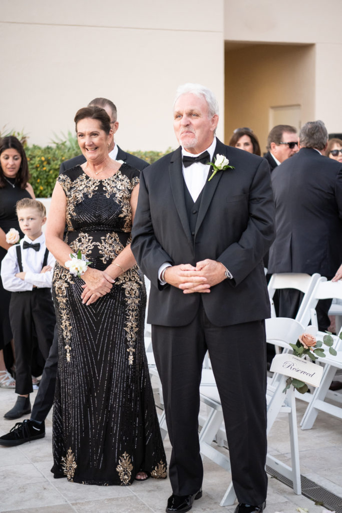 Mother and father of the bride smiling at bride and groom during wedding ceremony 