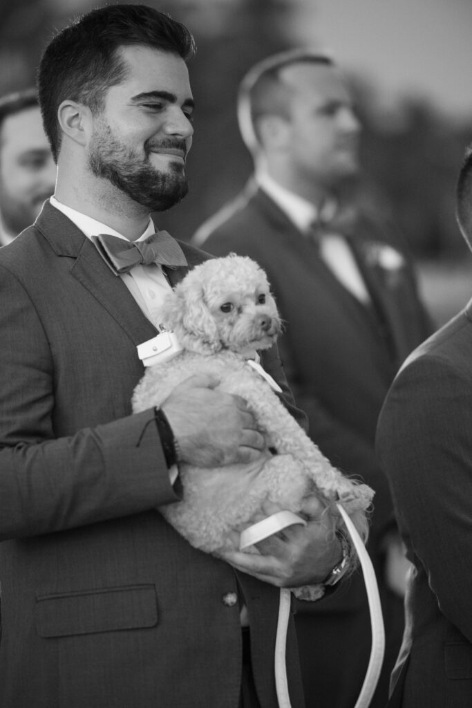 Groomsmen holding little dog during wedding ceremony on Florida beach 